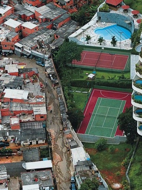 No lado esquerdo é vista várias casas em situações precárias e do lado direito um condomínio de luxo com um quadra de tênis